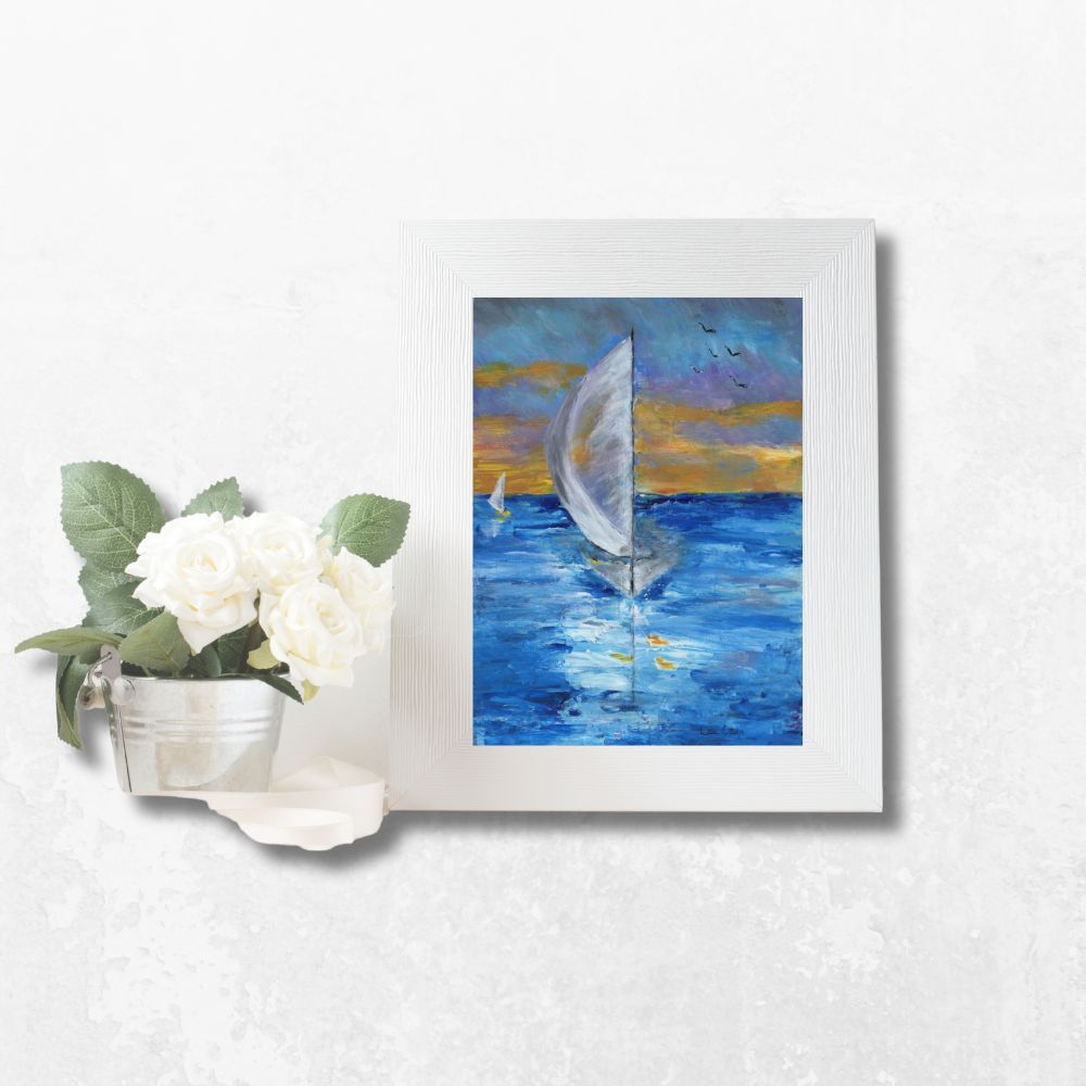 Greeting card framed on a table, featuring a white sailboat and sunset sky