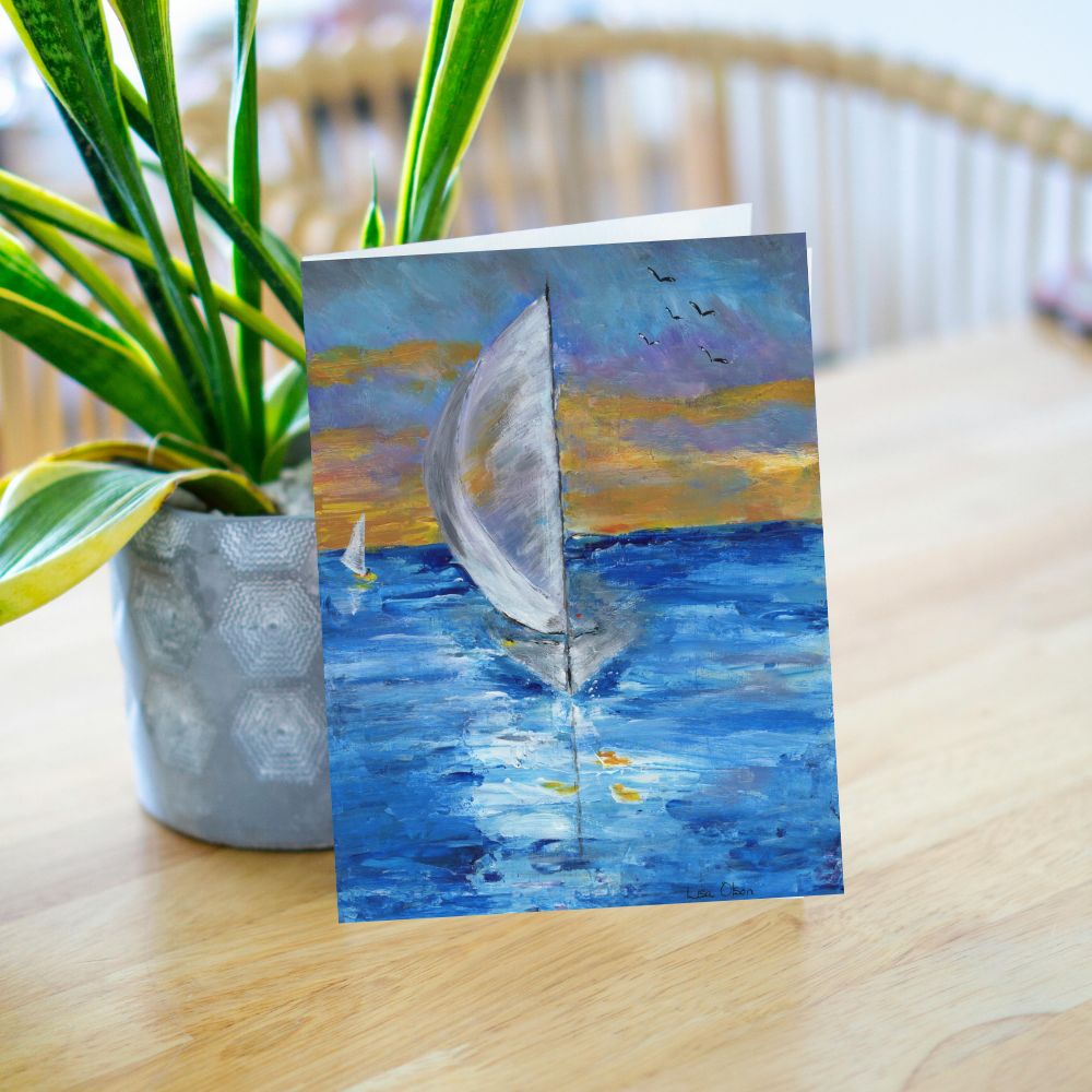 Greeting card with sailboat and sunset leaning against a plant on a table
